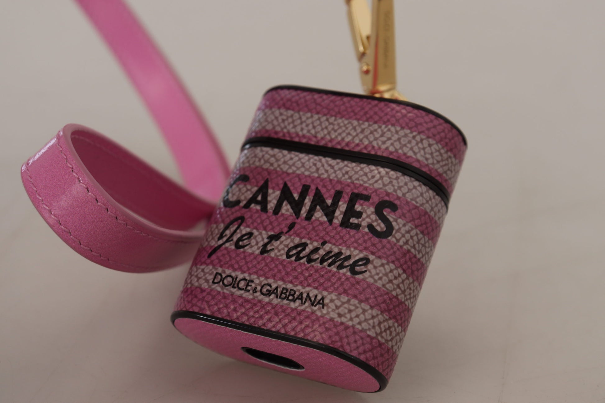 Étui Airpods en cuir rose et noir avec logo doré en métal.