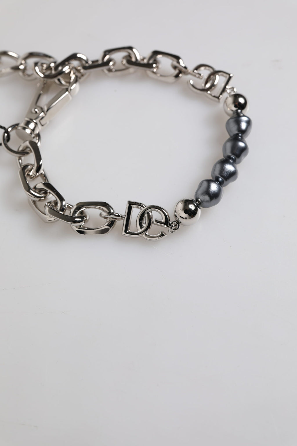 Bracelet en perles grises avec chaîne argentée, fermoir à crochet et logo.