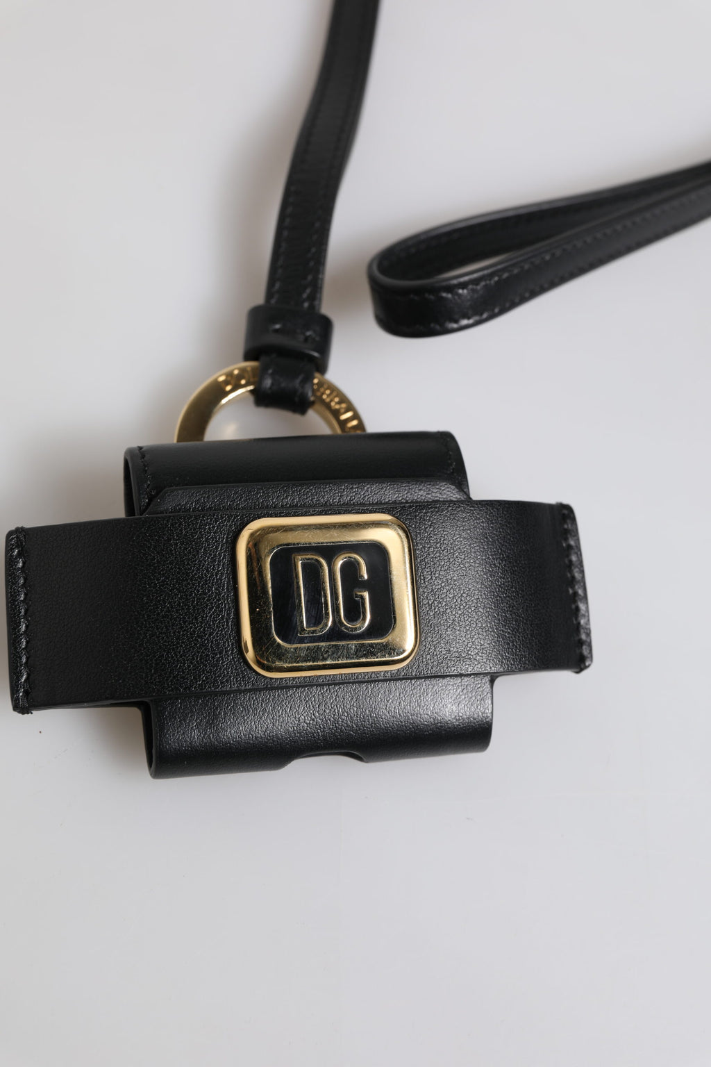 Étui Airpods en cuir noir avec plaque métallique dorée portant le logo.