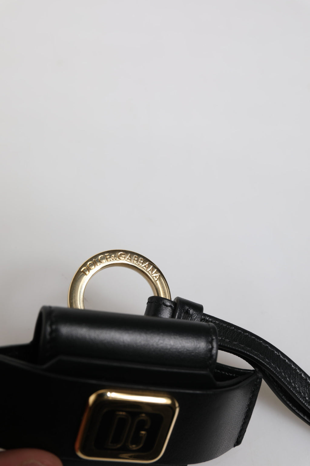 Étui Airpods en cuir noir avec plaque métallique dorée portant le logo.